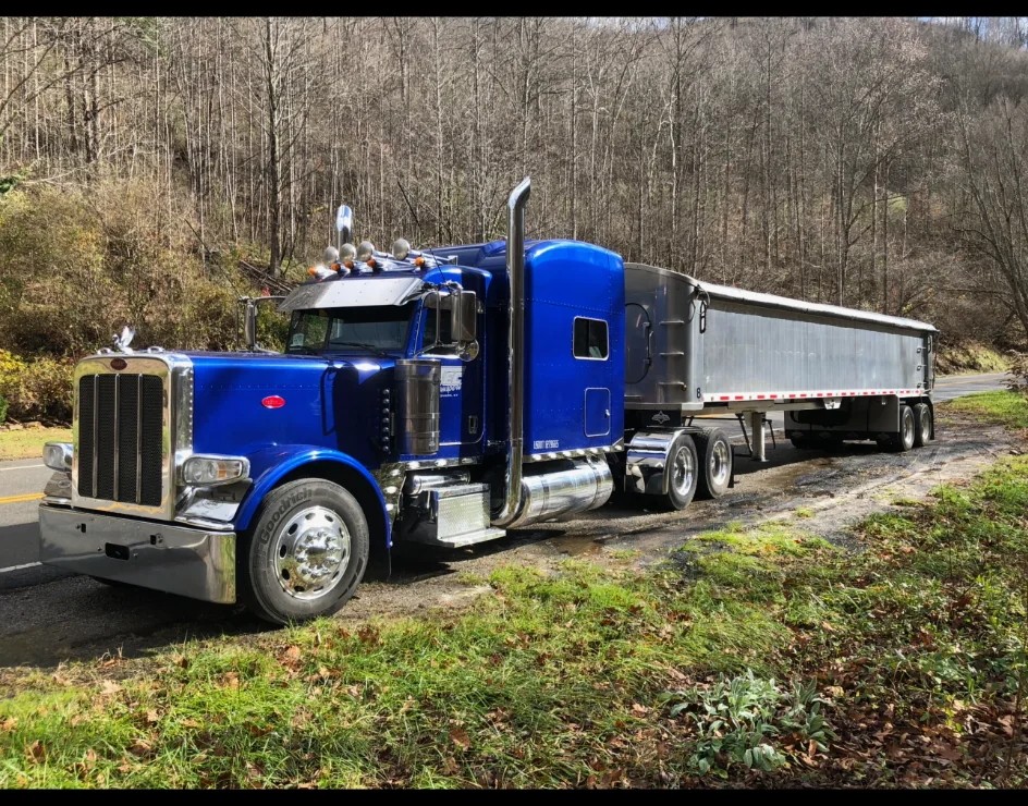 Blue Peterbilt semi truck pulling a dump trailer parked beside a road